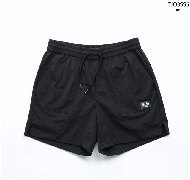 Quần short đen cạp chun dây rút, hai túi đắp phía trước, miếng logo nhỏ trên túi, xẻ tà hai bên, trải phẳng nền trắng