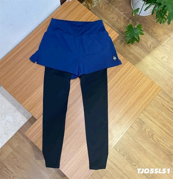 Quần legging đen phối short ngoài xanh navy xẻ hai bên, trải phẳng trên bàn gỗ, logo nhỏ ở gấu