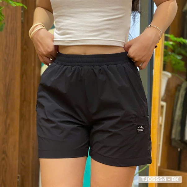 Quần short đen lưng chun mặc trên người, túi hộp bên đùi có nhãn logo, phối áo croptop trắng