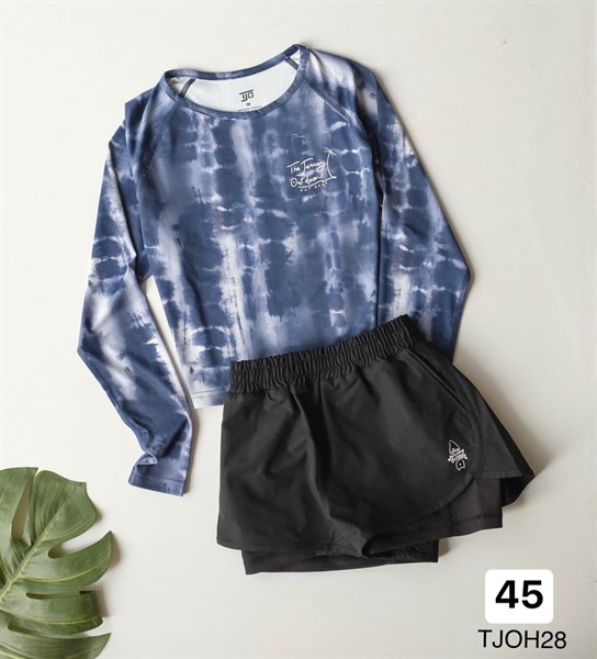 Áo croptop dài tay loang xanh navy trắng phối quần short đen hai lớp, trải phẳng trên nền trắng cạnh lá cây