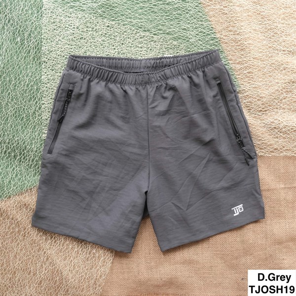 Quần short xám đậm trải phẳng trên nền lưới và bao tải, cạp chun, hai túi khoá kéo, logo nhỏ ở ống