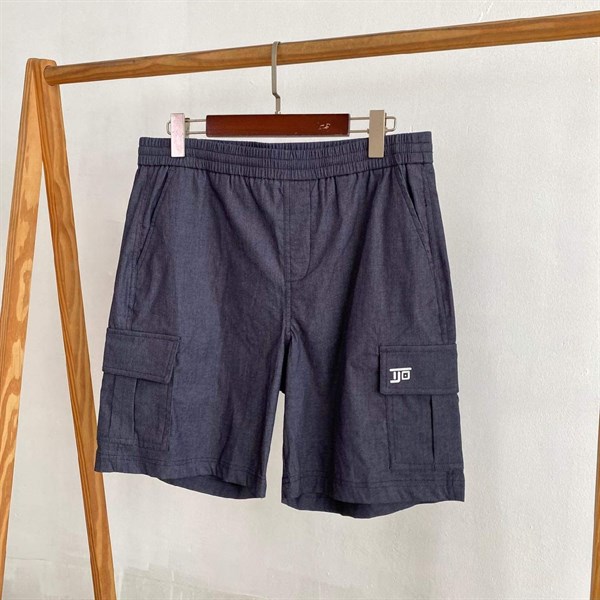Quần short túi hộp màu xanh navy đậm cạp chun treo trên giá gỗ, logo trắng trên nắp túi hông
